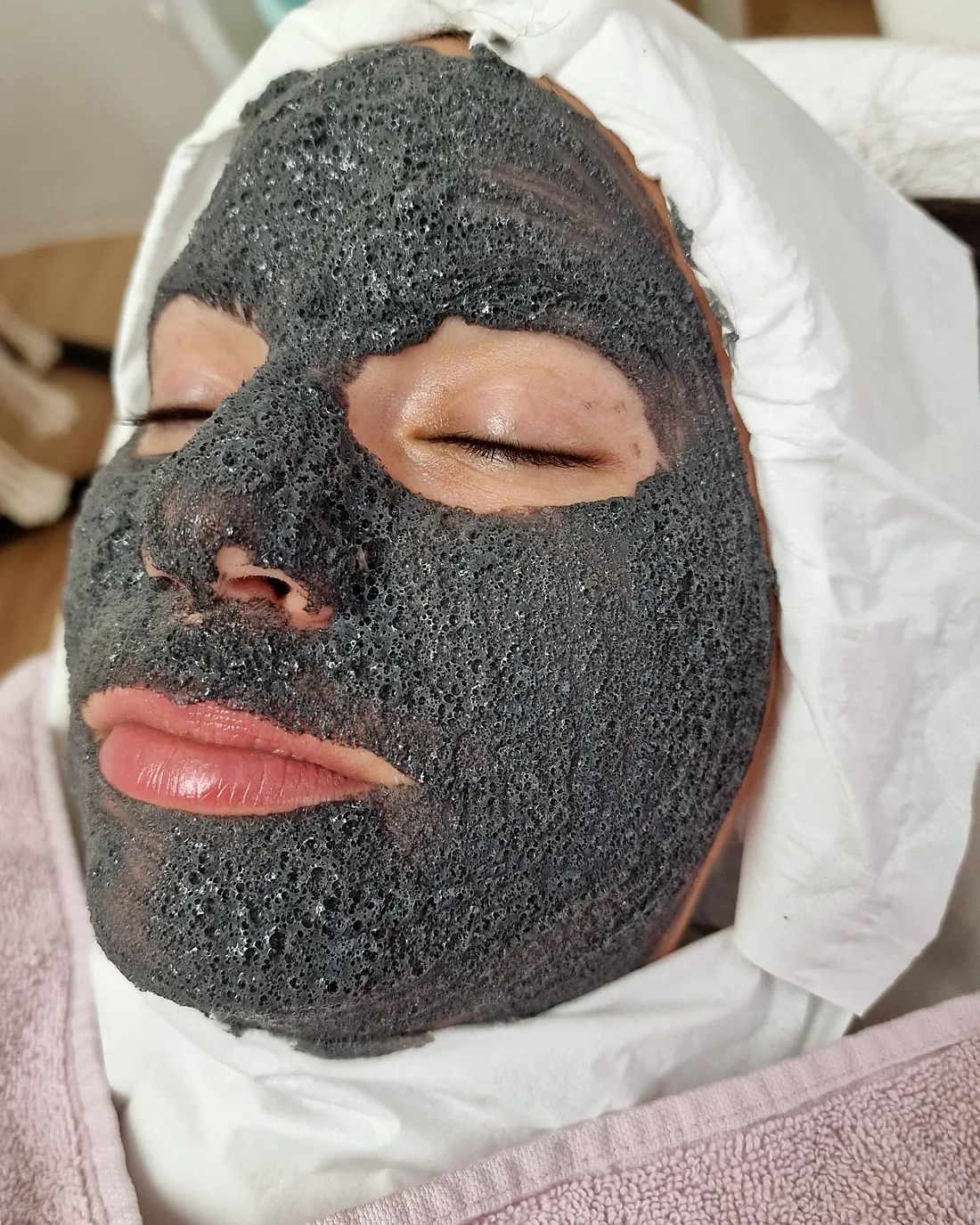 Kundin mit dunkler Maske aus Vulkanasche und Kohle während des Pure and Lift Treatments